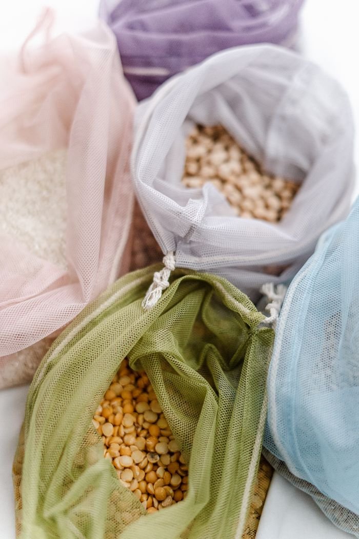 Assorted grains in colorful, reusable mesh bags on a white background.